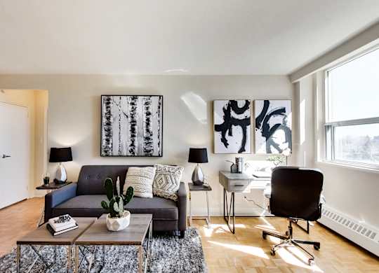 A living room with a grey couch, a black chair, a coffee table, and a painting on the wall.