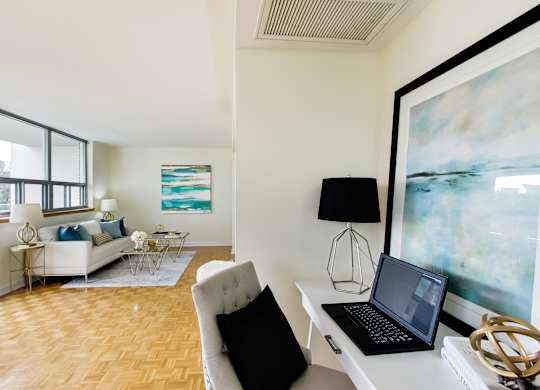 A laptop is on a desk with a lamp and a painting in the background.