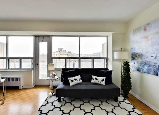 A black couch with white pillows sits in a living room with a large window.