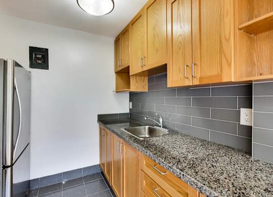 an empty kitchen with granite counter top and stainless steel refrigerator