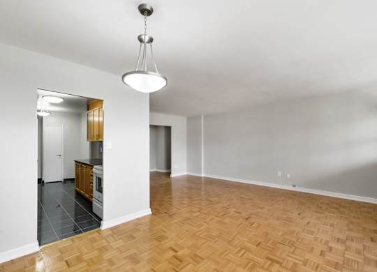 an empty living room with wood flooring and a kitchen
