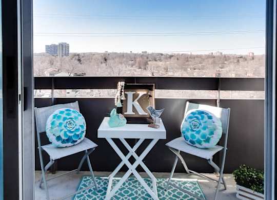 a balcony with three chairs and a table with two large pillows