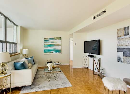A living room with a white couch, a glass coffee table, and a television.