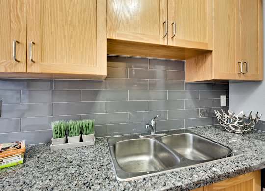 a kitchen sink with wood cabinets and gray tiles