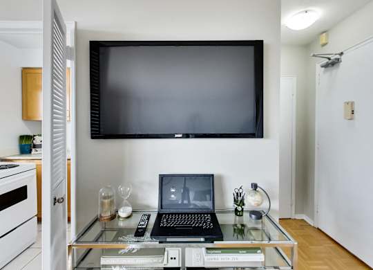 A black laptop is on a glass coffee table with a remote control and a book titled