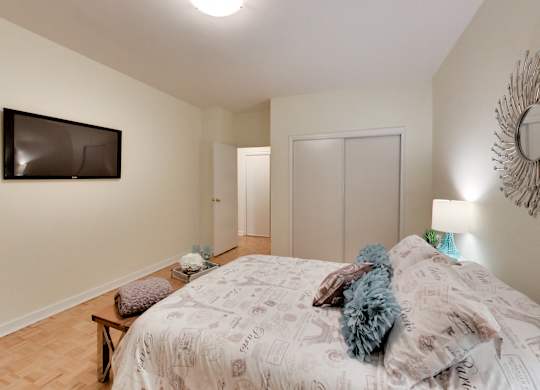 A bedroom with a bed, a bench, a mirror and a television.