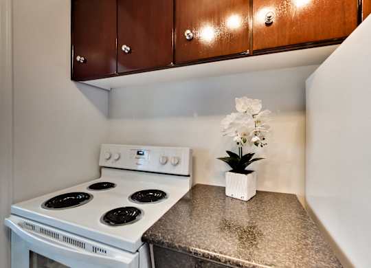 A white stove top oven with four burners and a white pot with white flowers on a granite counter.