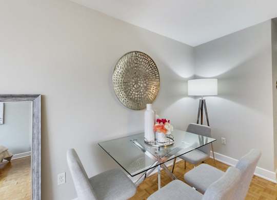 A dining room with a glass table and grey chairs.