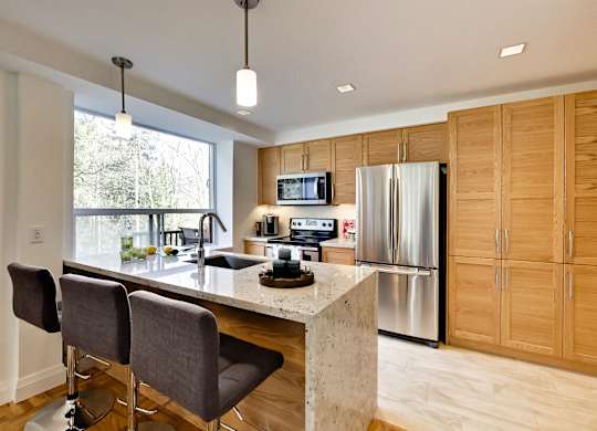 a kitchen with wooden cabinets and a marble counter top and a stainless steel refrigerator
