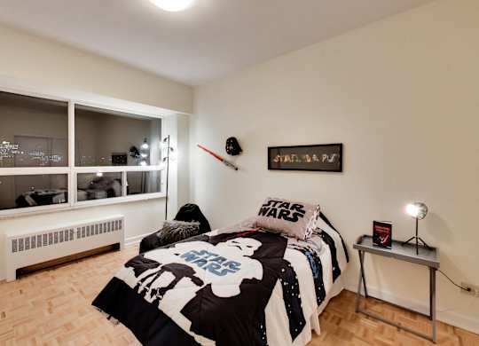 A Star Wars themed bedroom with a bed, a table with a lamp, and a poster on the wall.