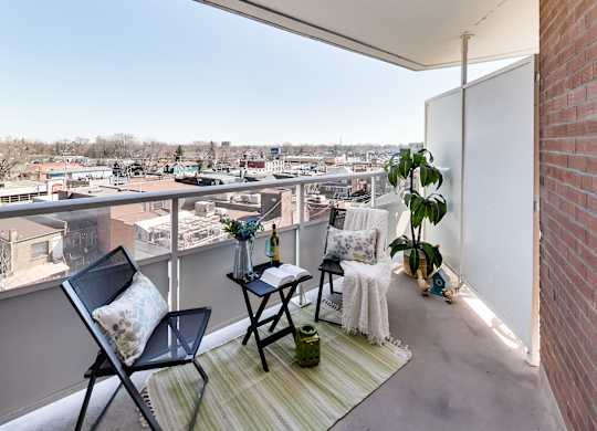 A balcony with a chair, table, and potted plant overlooking a cityscape.
