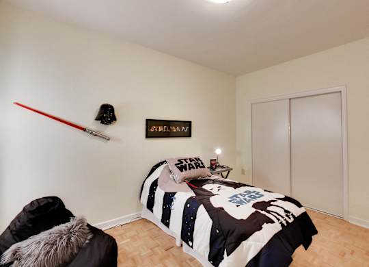 A bedroom with a bed, a chair, and a Star Wars poster on the wall.