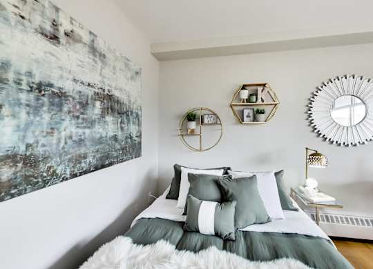 A bedroom with a large painting on the wall and a bed with a grey comforter.
