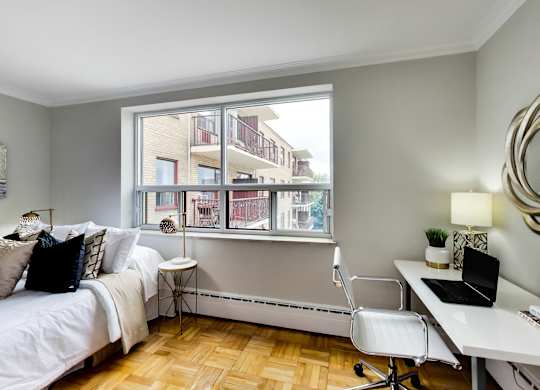 a bedroom with a large window and a bed and a desk with a laptop