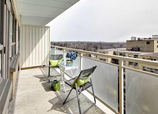 A balcony with a table and chairs overlooking a cityscape.