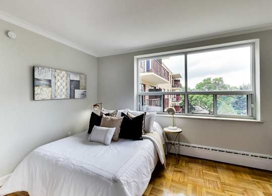 a bedroom with a large window and a bed with white sheets and pillows