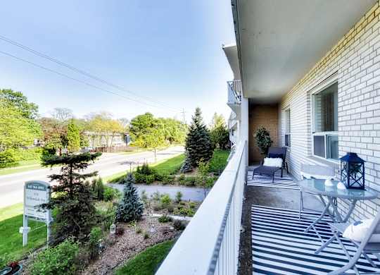 the view from the balcony of a white house with a patio and a garden