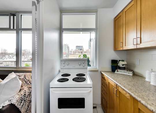 A white stove in a kitchen with wooden cabinets and a window.