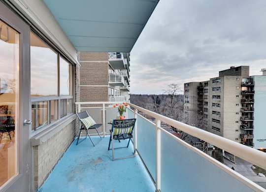 A balcony with a table and chairs overlooking a cityscape.