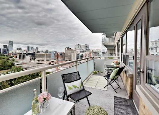 A balcony with a table and chairs overlooking a city skyline.