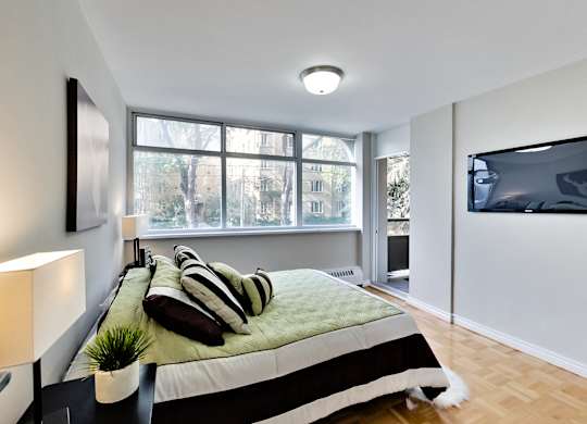 A bedroom with a bed, a chair, a lamp, and a window.