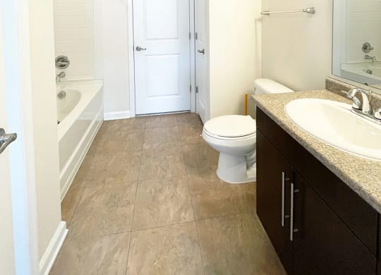 A white toilet sits in a bathroom next to a sink and a bathtub.