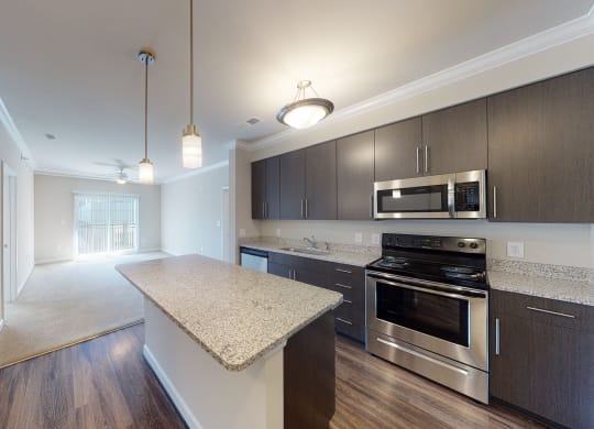 Kitchen with island, dark cabinets, vinyl floors and granite countertops; open to living room