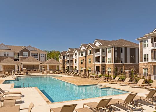 A large swimming pool surrounded by sun loungers and chairs in front of apartment buildings.