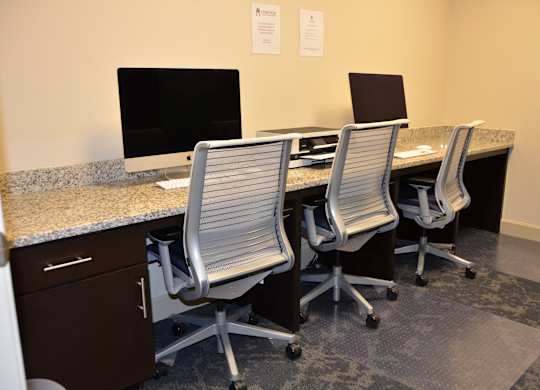 Three chairs are arranged around a desk with two computer monitors and a printer.