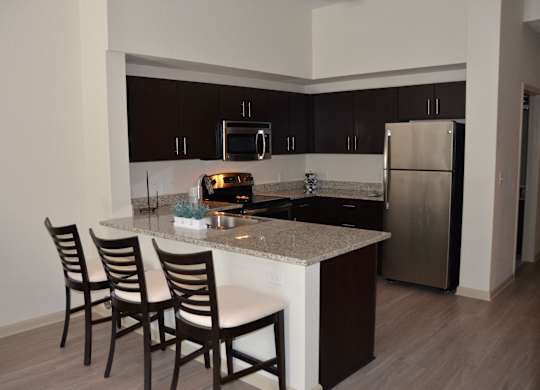 A kitchen with a white counter top and brown chairs.