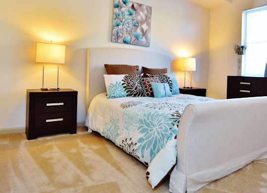 A bedroom with a large bed, two lamps, and a dresser.
