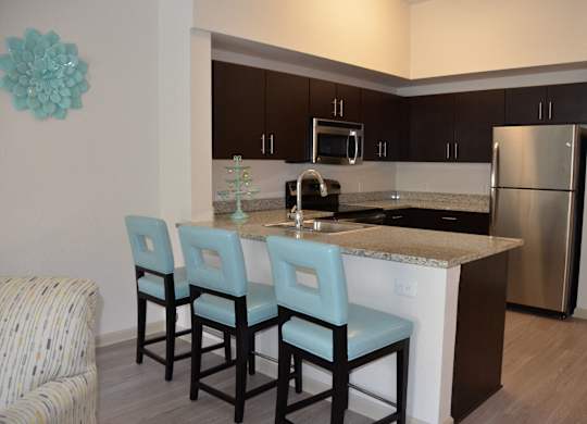 A kitchen with an island, three chairs, and a refrigerator.