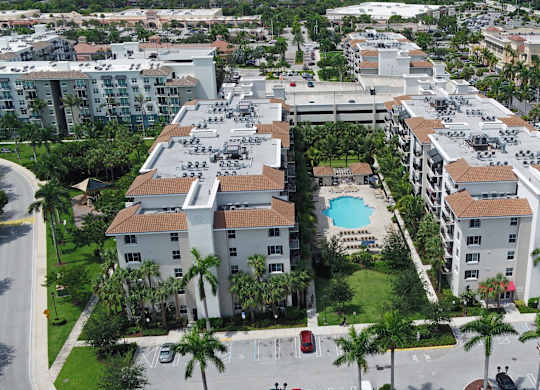 A large apartment complex with a pool in the middle of a courtyard surrounded by palm trees.