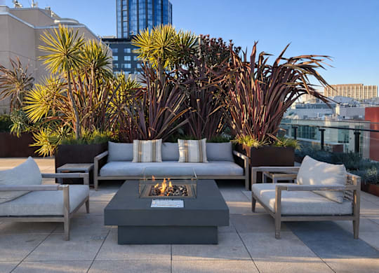 A patio with a fire pit surrounded by chairs and cushions.