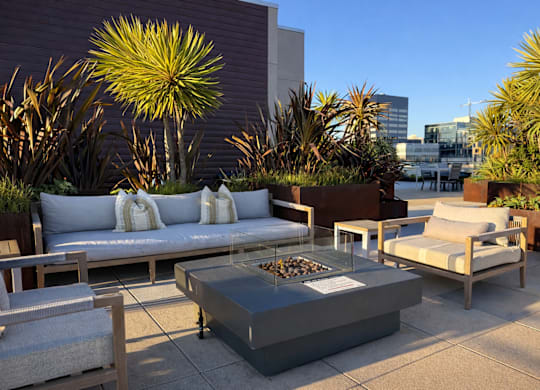 A patio with a couch, chairs, and a table with a fire pit in the middle.