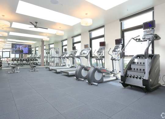 A spacious gym with a variety of equipment including treadmills, elliptical machines, and a television.