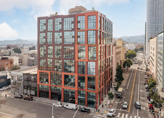 A tall red building with many windows is in the middle of a city street.