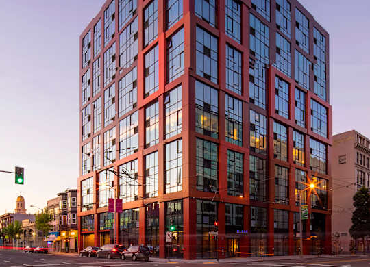 A tall red building with many windows stands in the middle of a street.