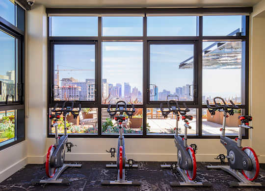 A gym with exercise bikes and a view of the city outside the window.