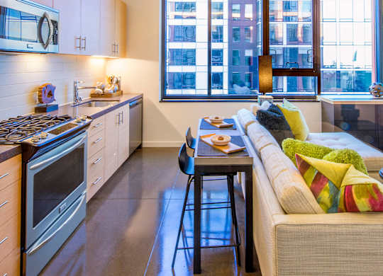 A modern kitchen with a bar stool and a couch with colorful pillows.