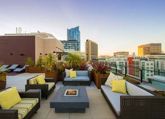A patio with a fire pit and couches overlooks a city skyline.