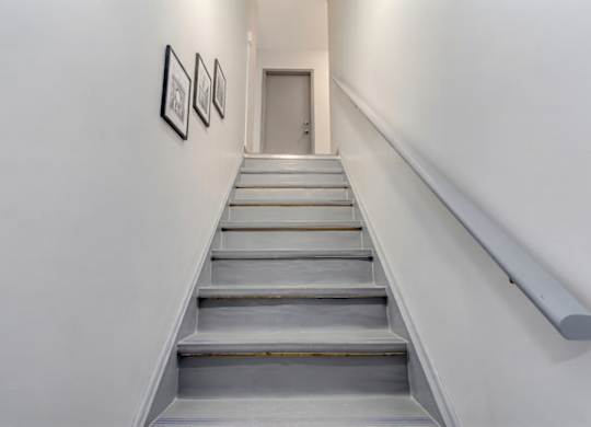 A staircase with a metal handrail and three pictures on the wall.