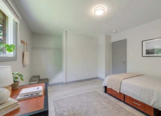 A bedroom with a bed, nightstand, and a window.