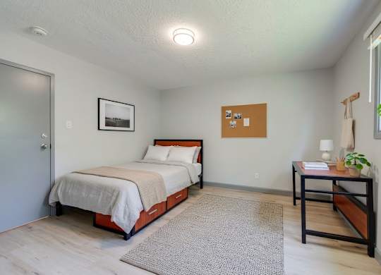 A bedroom with a bed, nightstand, and a table with a plant on it.