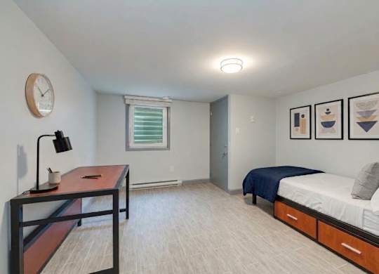 A bedroom with a bed, desk, and clock on the wall.