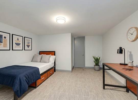 A bedroom with a bed, desk, and artwork on the wall.