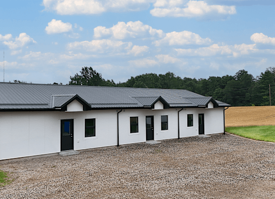 A white house with a black roof is surrounded by a gravel driveway.
