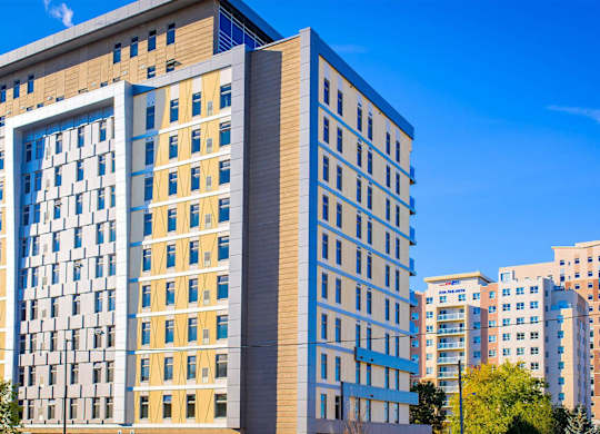 A modern multi-story building with a blue and yellow facade stands under a clear blue sky.