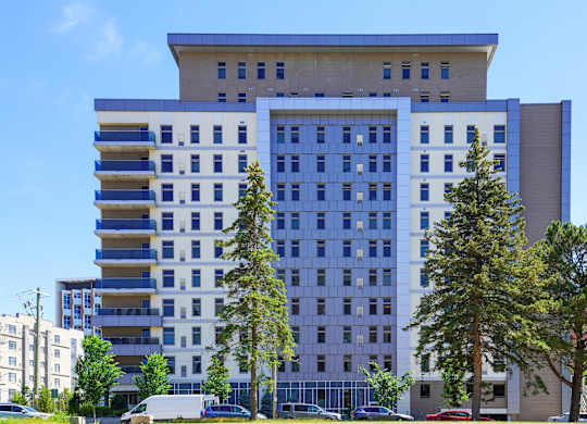 A large building with a blue and white facade is surrounded by trees and cars.
