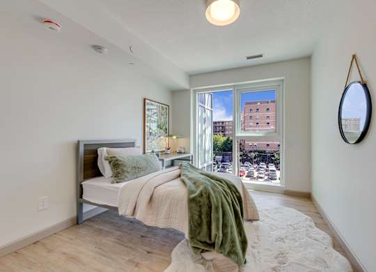 A bedroom with a bed, a mirror, and a window overlooking a city street.